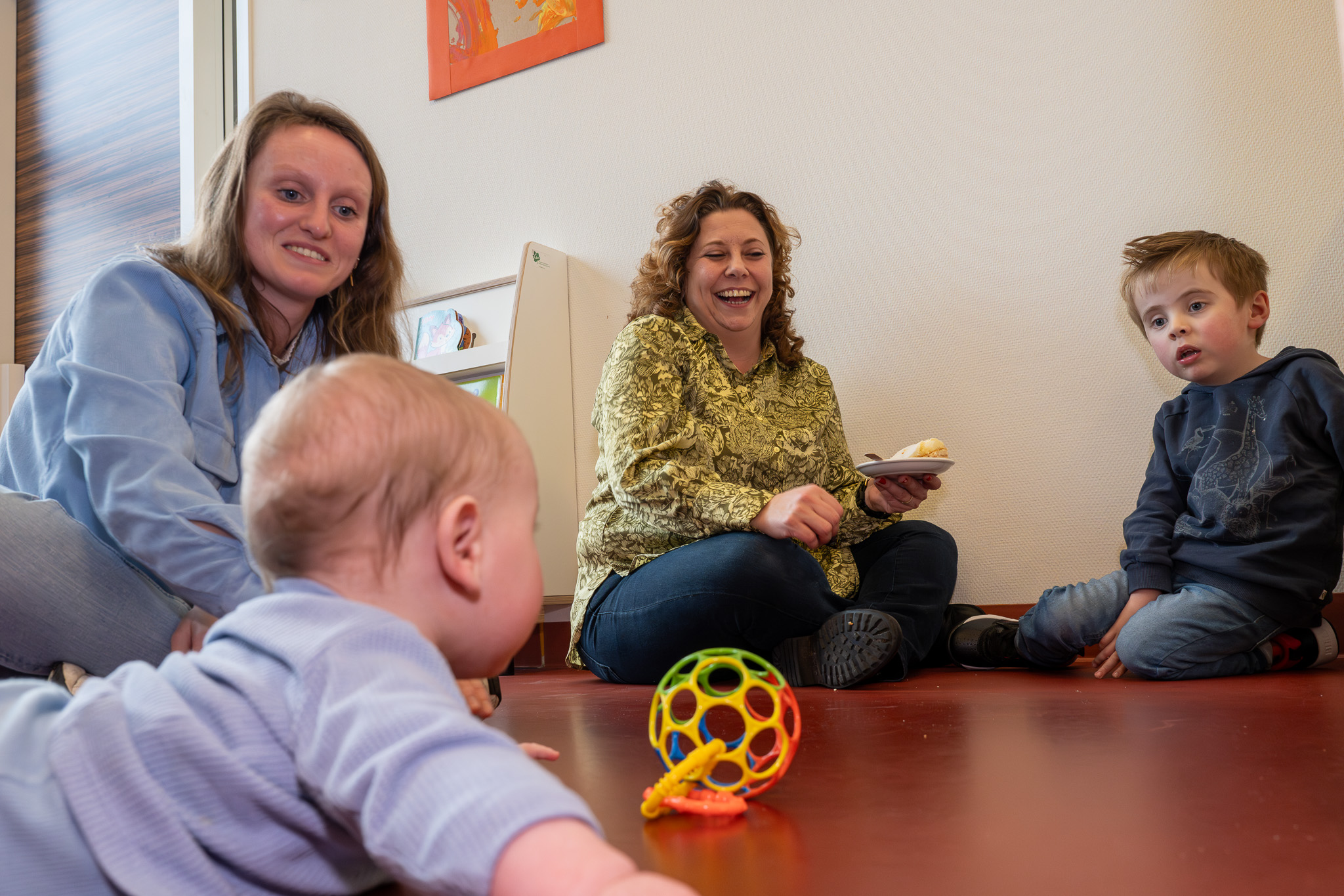 Een baby en een peuter kijken naar en spelen met elkaar. Hun moeders kijken toe.