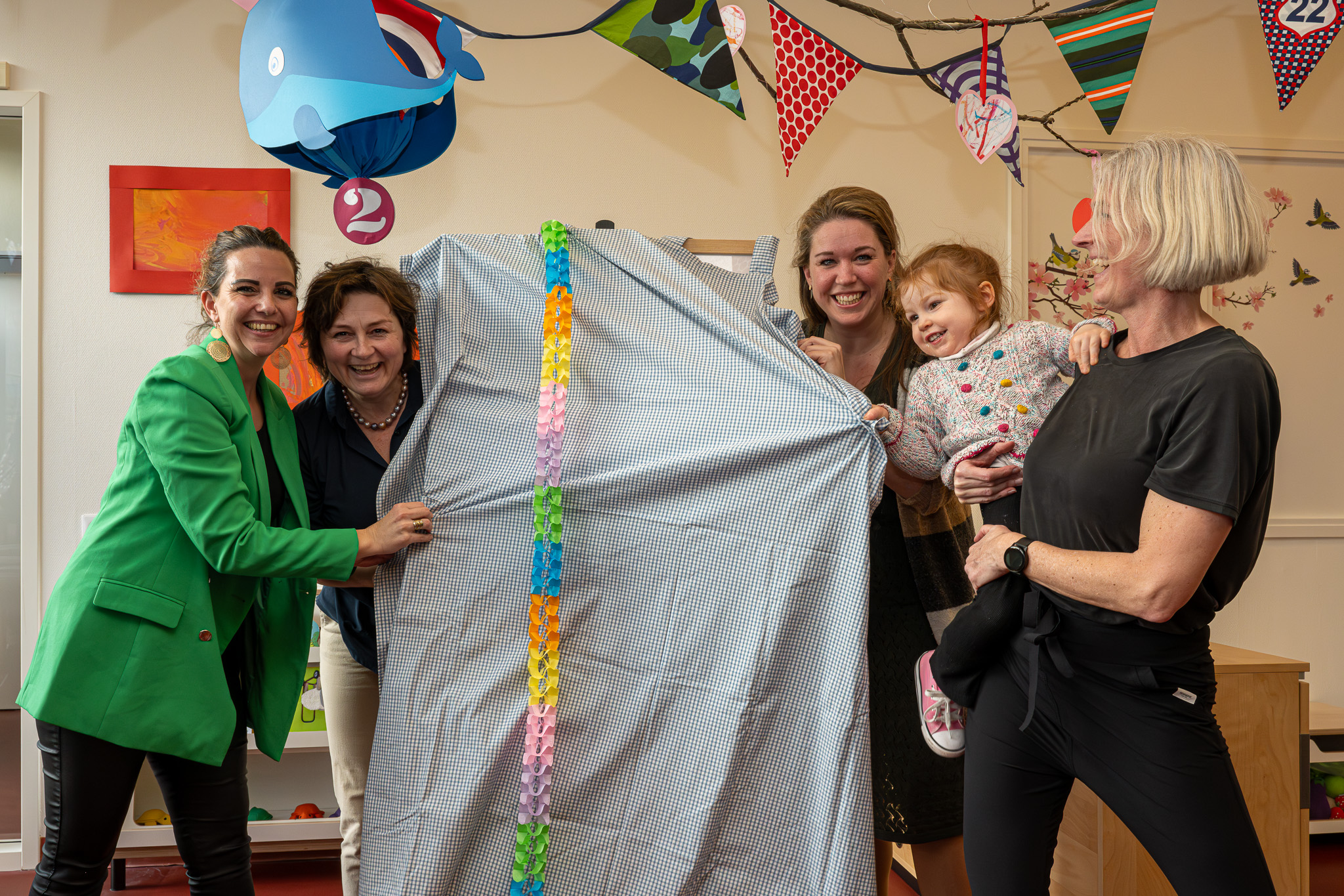 Izabella (3), pedagogisch medewerker Mathilde en de bestuurders van 2Samen, Kombino en Basalt staan klaar om het doek over het zelfgemaakte kunstwerk eraf te trekken