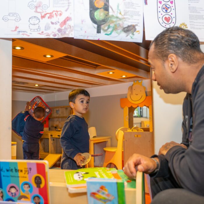 Twee jongens spelen in de huishoek bij Peuteropvang 2Acrobaten in Morgenstond. Pedagogisch medewerker komt bij hen kijken.