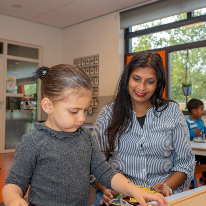 Pedagogisch medewerker kijkt hoe een peuter bij 2Acrobaten haar puzzelt met succes maakt.