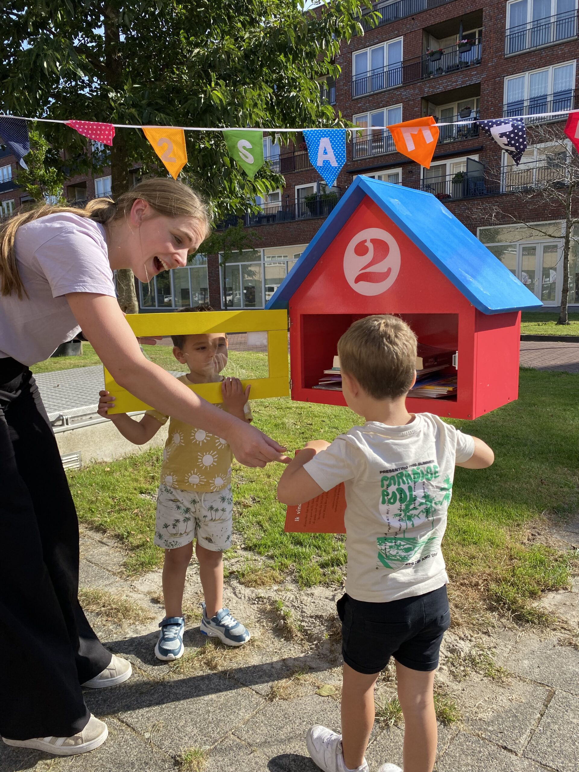 Twee peuters laten enthousiast aan een pedagogisch medewerker de mini-bieb met boekjes zien bij kdv 2Eekhoorns in Hoogeland Naaldwijk